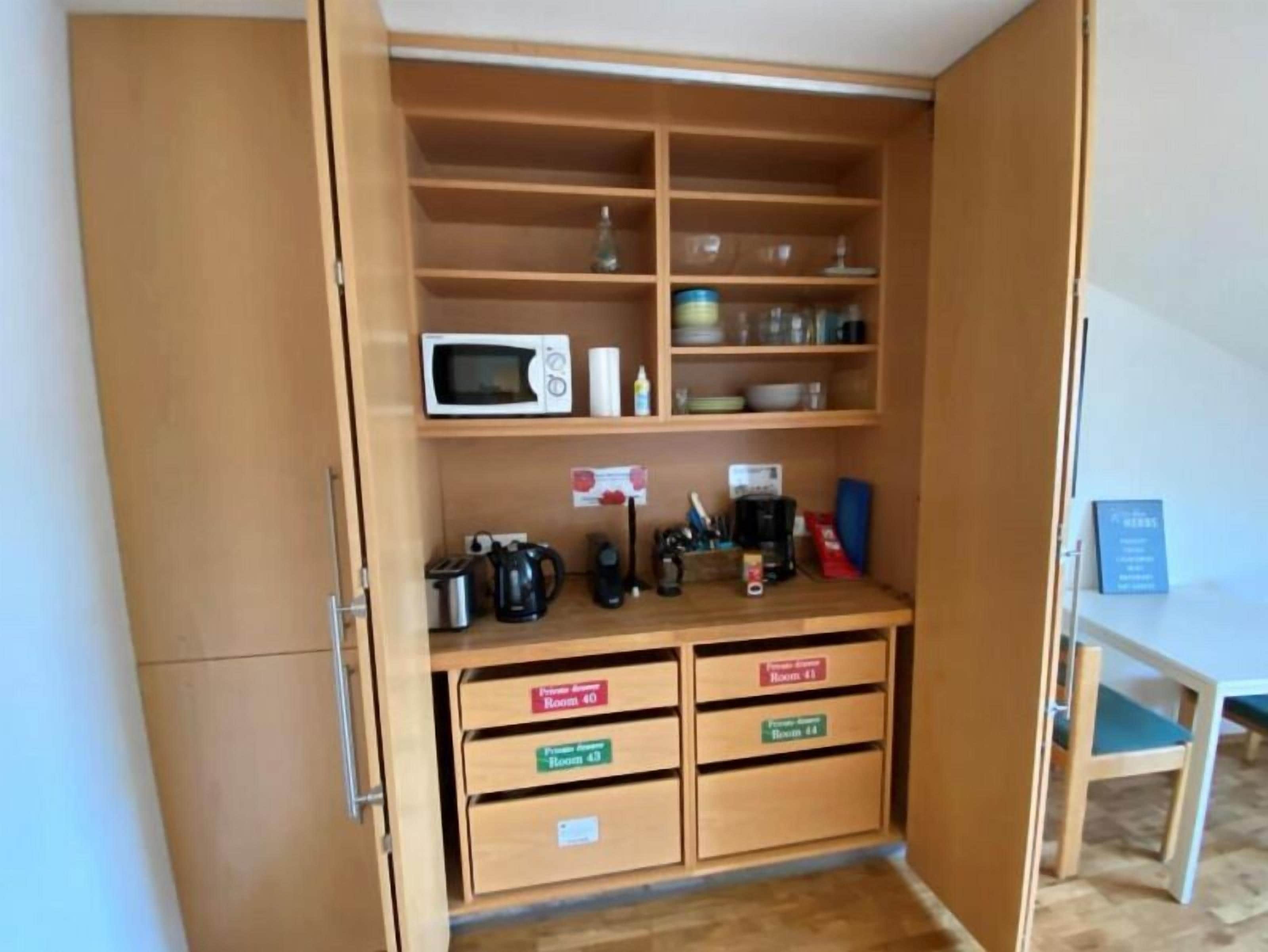 Een kleine keuken met een magnetron, koffiezetapparaat en opbergladen voorzien van kamer nummers.