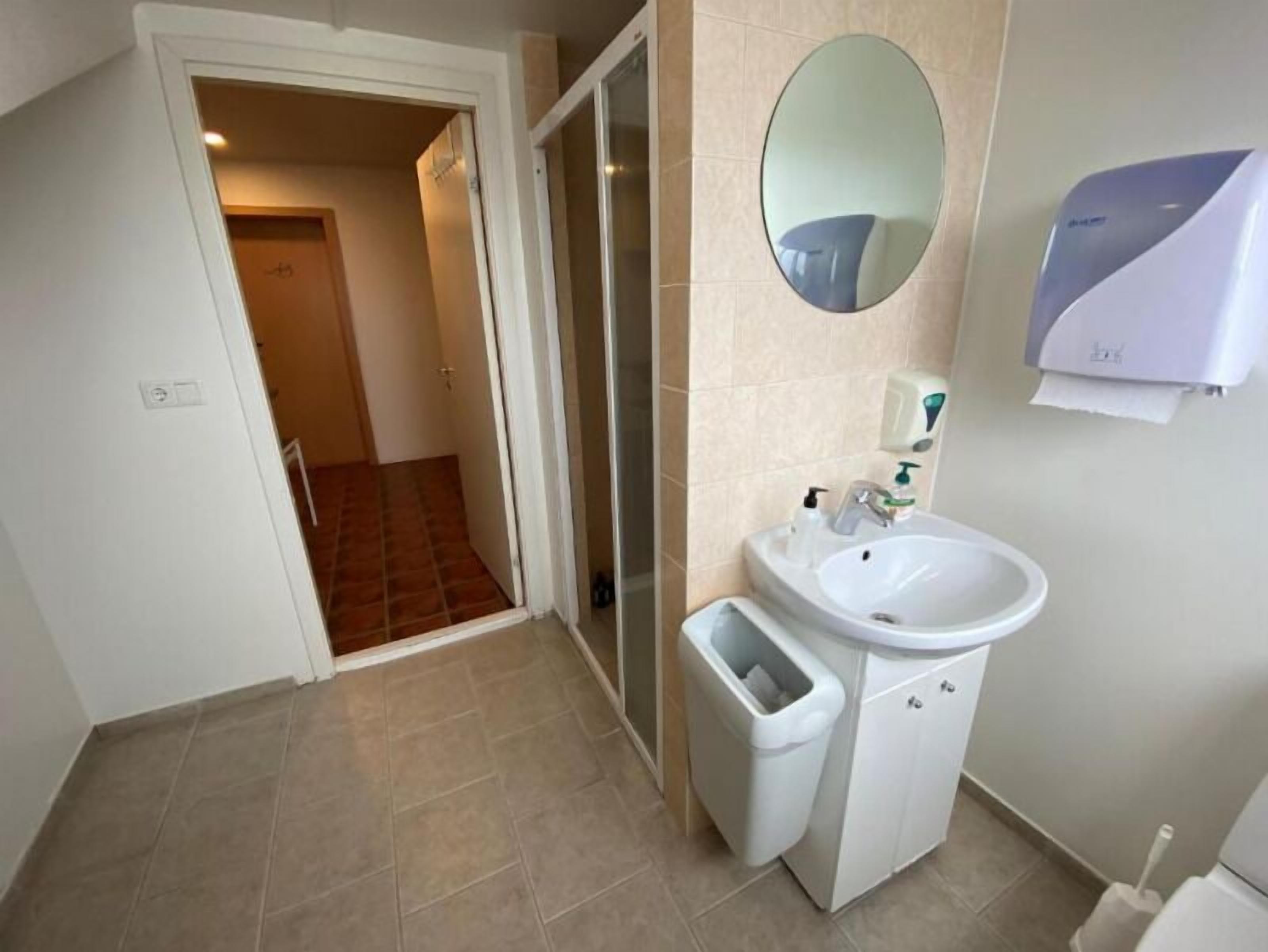 Un baño con lavamanos, espejo y secamanos.
