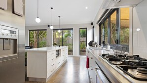 Cocina moderna con una isla central, electrodomésticos de acero inoxidable y ventanas amplias con vistas al jardín.