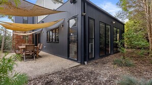 Una casa moderna con un patio que cuenta con una mesa y sillas, ventanas amplias y un espacio al aire libre con sombra.