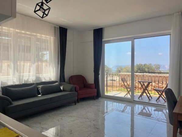 A modern living room with a sofa, a red armchair, and a balcony with a view.