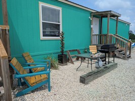 Un edificio verde con terraza de madera, mobiliario exterior y zona de barbacoa.