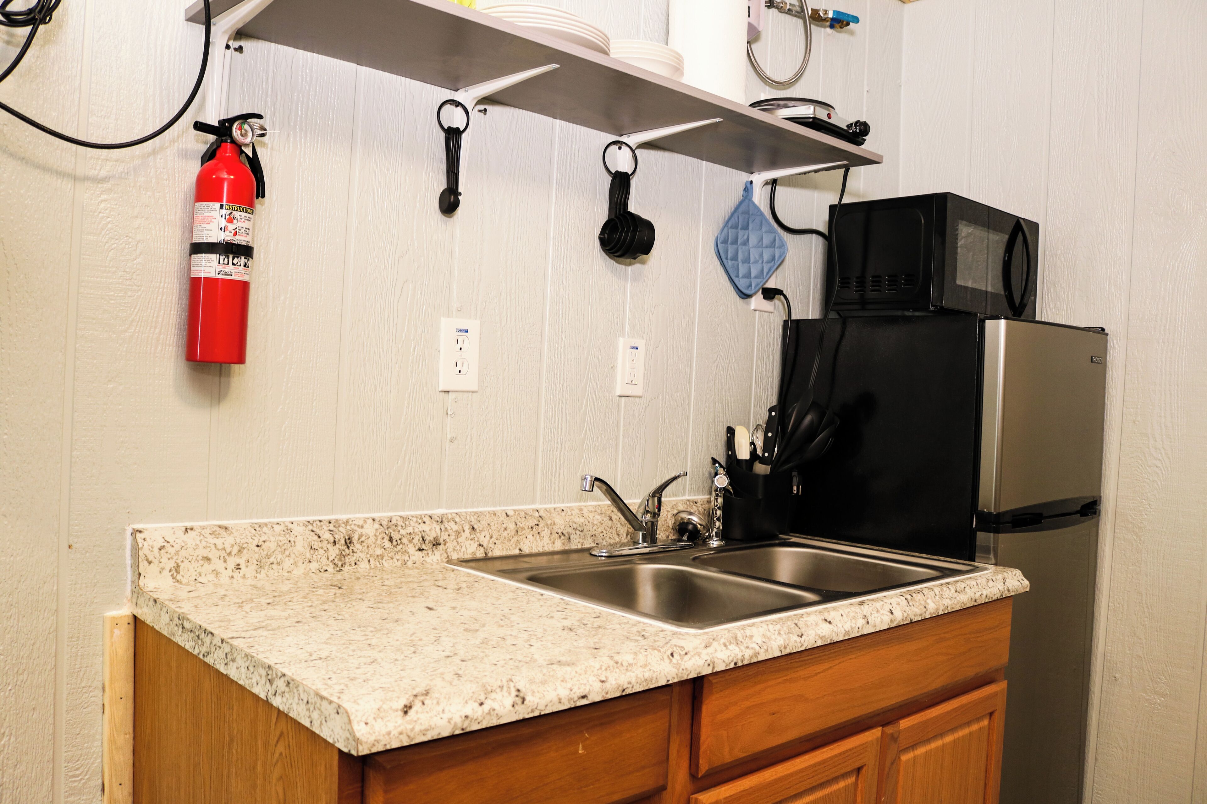 A kitchen with granite countertops, stainless steel sinks, a black microwave, and a stainless steel refrigerator.