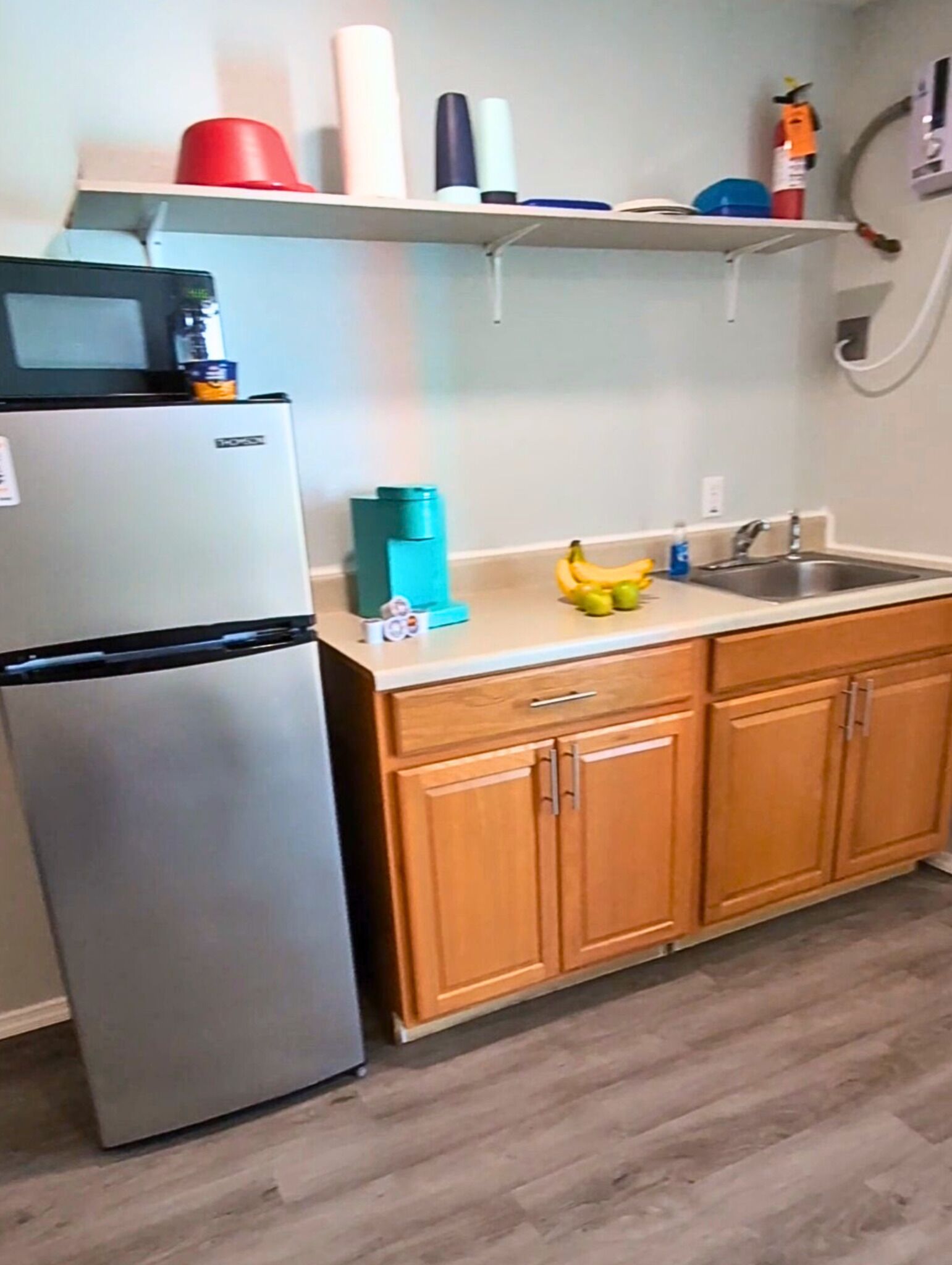 Una cocina compacta con refrigerador, armarios de madera, un lavamanos y una encimera.
