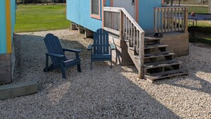 A small blue cabin with a white door, a wooden deck, and two Adirondack chairs. - Simple Stay (Port Lavaca)
