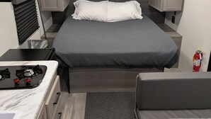 A compact RV interior with a bed, kitchenette, and seating area. - Simple Stay (Port Lavaca)