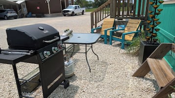 Grill, bord og udendørs møbler med træterrasse, og en varevogn parkeret i nærheden.