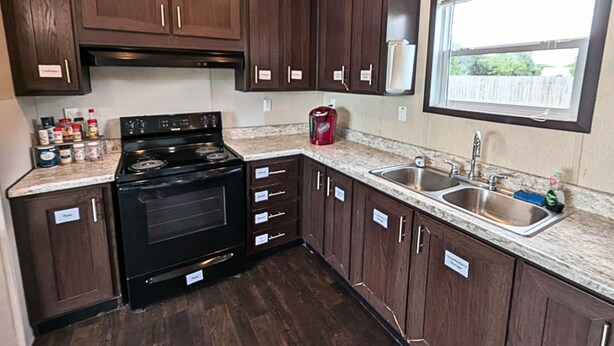 A kitchen with dark wood cabinets, a black stove, and a granite countertop. - Simple Stay (Port Lavaca)