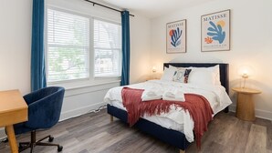 Un dormitorio con cama, escritorio y dos cuadros.