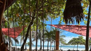 Eine Sitzgelegenheit am Strand mit Holztischen und -stühlen, einer Tiki-Bar und Blick auf den Ozean.