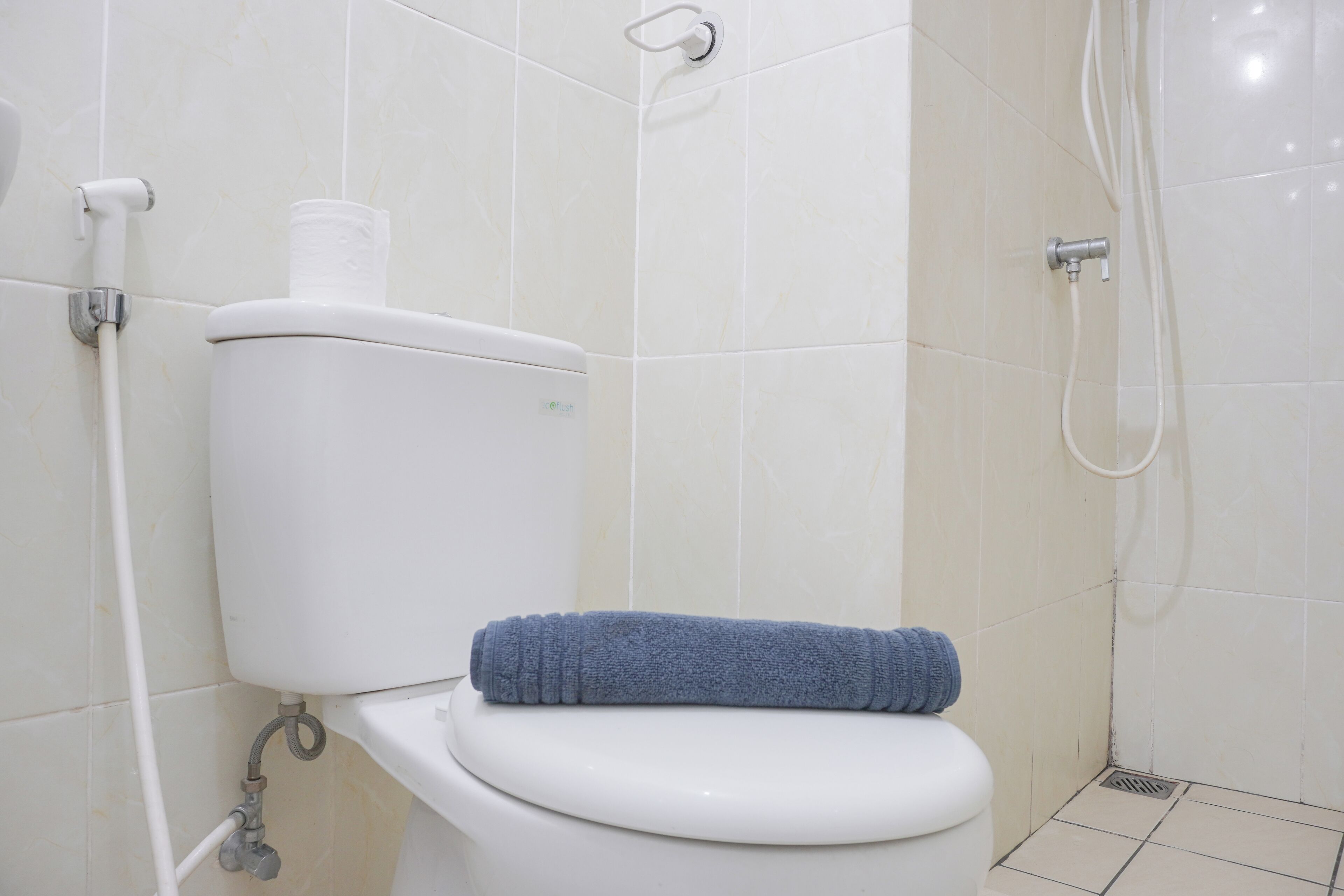 Un baño con un inodoro blanco, una toalla azul sobre el asiento y una zona de ducha con manguera.