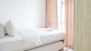 Ein ordentlich bezogenes Bett mit weißen Leinen und Kissen, ein Holzschrank und ein Fenster mit Vorhängen.