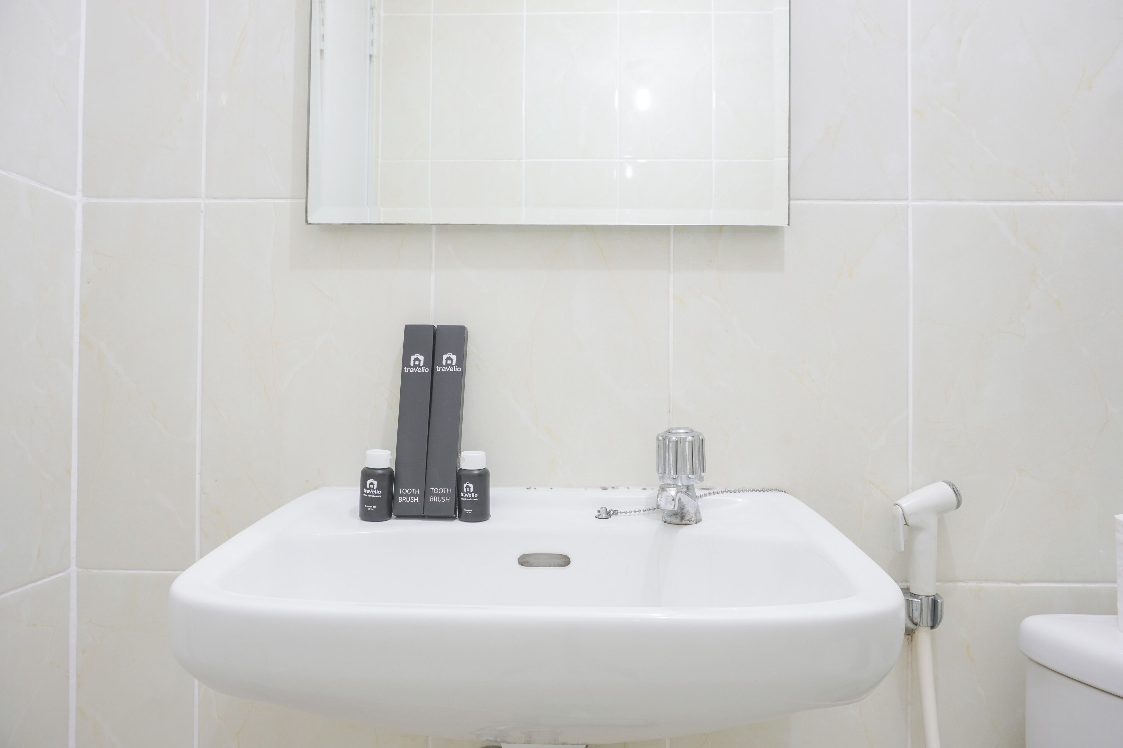 A white bathroom sink with a mirror above it, a toothbrush holder with two toothbrushes, and a small bottle of toothpaste.
