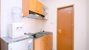 Een kleine keuken met een koelkast, een waterdispenser, een fornuis en houten kastjes.
