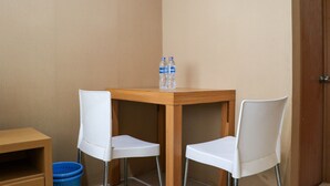 A corner room with a wooden table and two white chairs, a blue basket, and two water bottles on the table. - Modern And Nice Studio At Titanium Square Apartment (Jakarta)