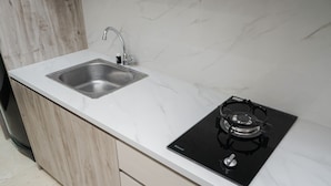 A modern kitchen with a stainless steel sink, a black induction cooktop, and wooden cabinetry. - Elegant Studio Apartment At High Floor B Residence (Pagedangan)