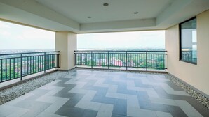 Un balcon spacieux doté d’un sol carrelé et d’une balustrade, offrant une vue sur le paysage urbain.