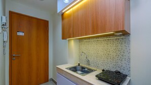 A small kitchen with a wooden door, a sink, and a tiled backsplash. - Comfy Studio At Evenciio Margonda Apartment (Depok)