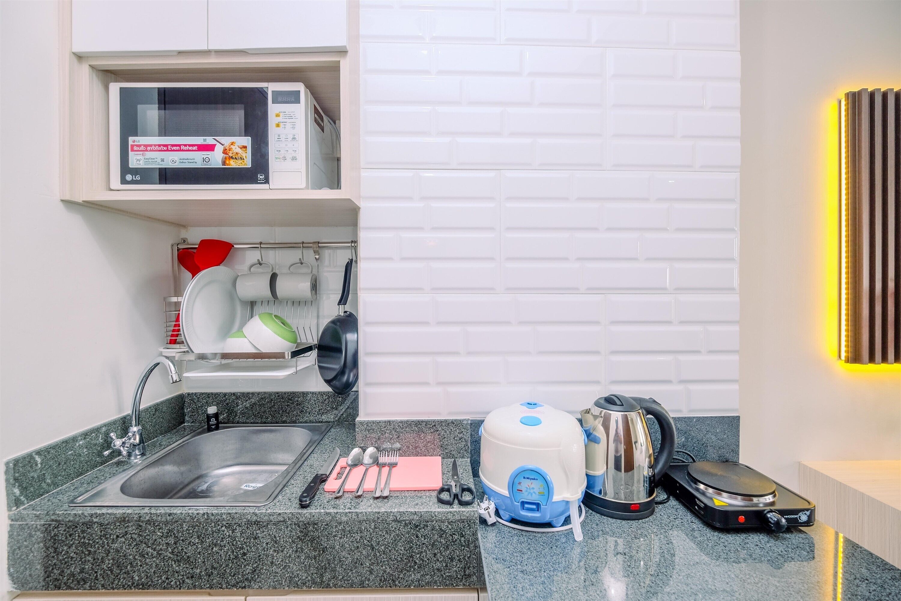 A compact kitchen with a sink, microwave, kettle, and a coffee machine.