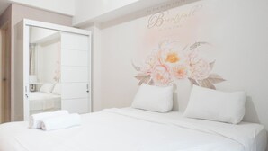 A hotel room with a large bed, white bedding, a mirror, and a floral wall decoration.