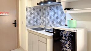 A compact kitchen with a sink, a microwave, and a cabinet with a floral design. - Homey 2Br At Meikarta Apartment (Cikarang)