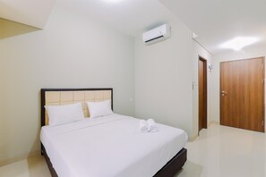 A neatly made bed with white linens and two rolled towels, a wooden door, and an air conditioning unit on the wall. - Homey Studio At Lrt City Sentul - Royal Sentul Park Apartment (Bogor)