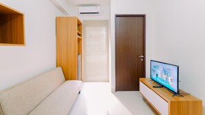 A modern living room with a sofa, a TV on a wooden stand, and a door. - Great Location And Comfy 2Br Transpark Cibubur Apartment (Depok)