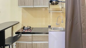 A compact kitchen with wooden cabinets, a sink, and a countertop with a kettle and a small appliance.