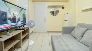 A living room with a television, a fan, a grey sofa, and a white door.