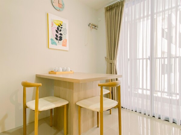 Un coin repas avec une table en bois et deux chaises, une horloge au mur et une fenêtre avec des rideaux.