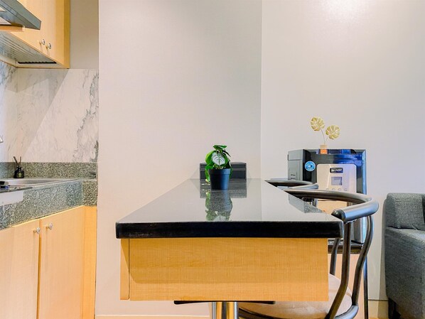 A modern kitchen with a marble backsplash, a black countertop, and a built-in stove. There is a small potted plant on the countertop and a coffee machine on the right side. - Modern Look 2Br At Transpark Cibubur Apartment (Depok)