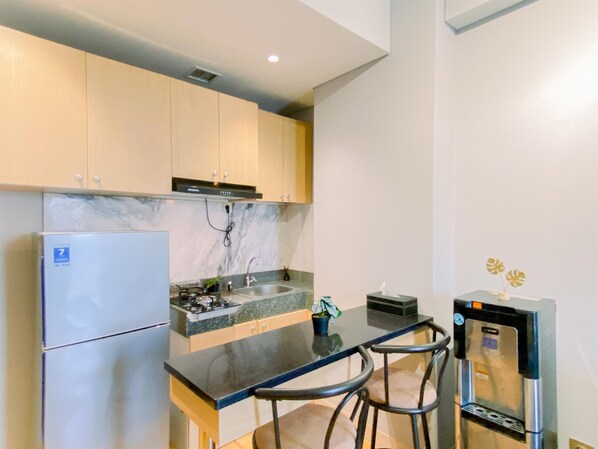 A compact kitchen with a refrigerator, stove, sink, and a water dispenser.