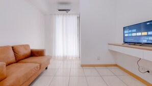 Ένα σύγχρονο σαλόνι με έναν καναπέ, μια τηλεόραση επίπεδης οθόνης και ένα παράθυρο με κουρτίνες.