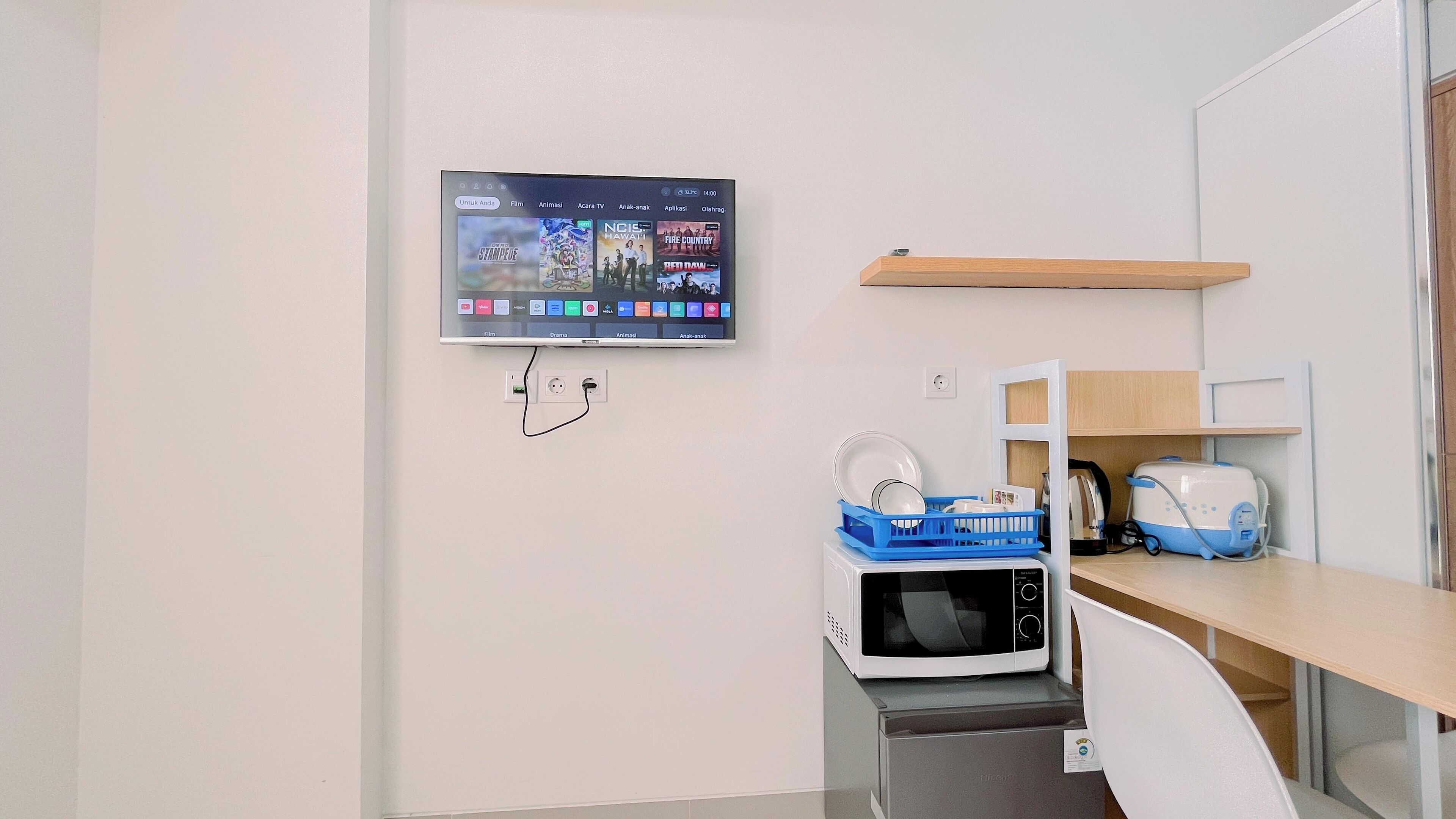 A modern hotel room with a flat-screen TV mounted on the wall, a microwave, a toaster, and a blue dish rack on the counter.