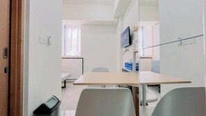 Et lille, moderne værelse med en trædør, et hvidt skrivebord, en stol og et fjernsyn på væggen.