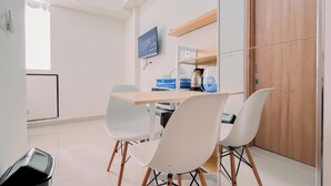 A modern dining area with a wooden table, white chairs, a television mounted on the wall, and a wooden door.