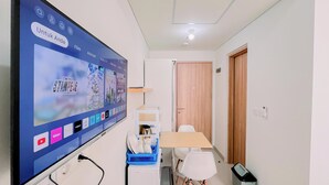 A room with a large TV displaying a streaming service interface, a wooden door, a white chair, and a small table with a blue dish rack.