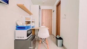 A compact kitchenette with a microwave, toaster, and small fridge. A white chair is positioned in front of a wooden door.