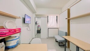 A compact hotel room with a bed, a desk, a chair, a TV mounted on the wall, and a window with a curtain. - Relaxing Studio (No Kitchen) Apartment Bandaraya - Tallasa City Makassar (Makassar)