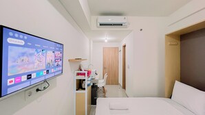 A hotel room with a TV displaying a movie selection, a desk with a chair, a wooden door, and a bed with white linens. - Relaxing Studio (No Kitchen) Apartment Bandaraya - Tallasa City Makassar (Makassar)