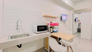 A compact kitchenette with a white sink, a microwave, a small table, and a chair. - Relaxing Studio (No Kitchen) Apartment Bandaraya - Tallasa City Makassar (Makassar)