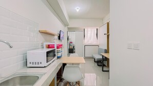 A compact kitchen with a microwave, sink, and a small dining area with a table and chairs. - Relaxing Studio (No Kitchen) Apartment Bandaraya - Tallasa City Makassar (Makassar)
