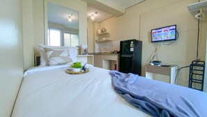 Ein Hotelzimmer mit Bett, einer kleinen Küchenzeile, einem Kühlschrank, einem Fernseher und einem Fenster mit Jalousien.