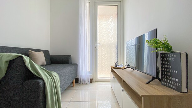 Een moderne woonkamer met een grijze bank, een houten tv-meubel en een bord met steden.