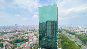 A modern high-rise building with a glass facade, surrounded by a densely populated urban area with various buildings and a clear sky.