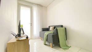 A modern living room with a grey sofa, a wooden desk with a computer and papers, and a green throw blanket.