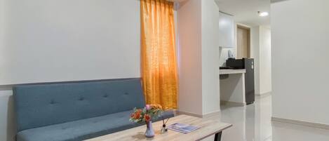 A modern living room with a blue sofa, a wooden coffee table with a vase of flowers, and a kitchen area in the background.