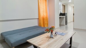 A room with a bed, a wooden table with a vase of flowers, and a desk with a computer. - Simple 2BR at Meikarta Apartment (Cikarang)