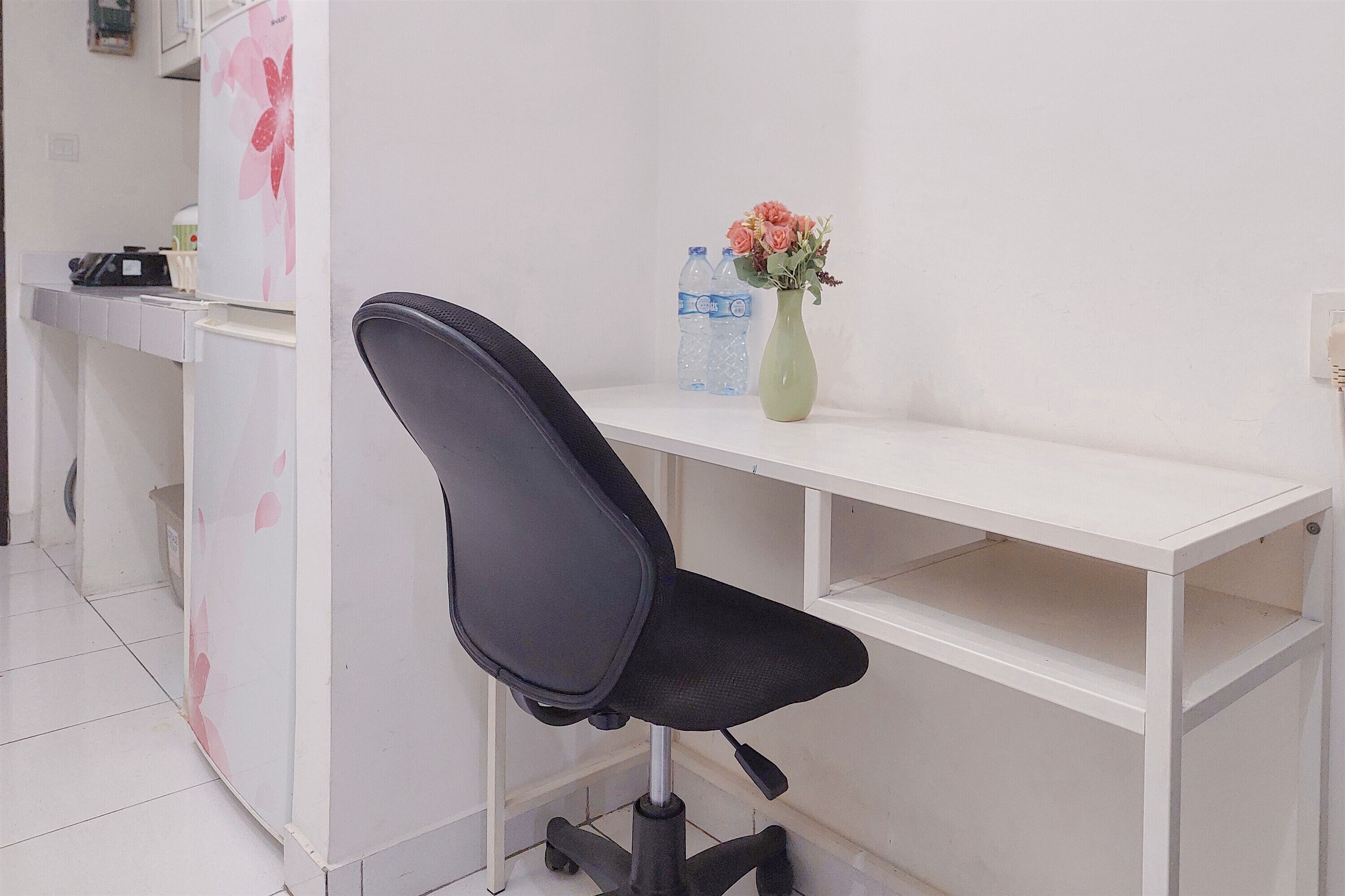 A white desk with a black office chair, a vase with flowers, and two water bottles.