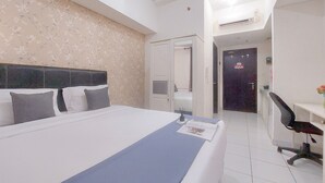 A hotel room with a large bed, a desk with a chair, and a bathroom visible through an open door. - Comfy And Well Furnished Studio Casa De Parco Apartment (Pagedangan)